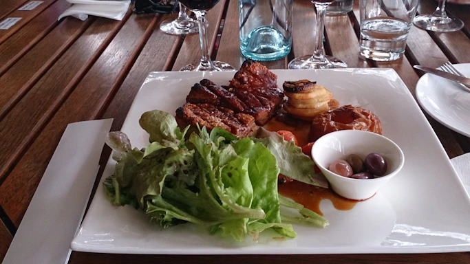 A rustic wooden table with a plate of Spanish tortilla, a small bowl of olives, and a glass of red wine.