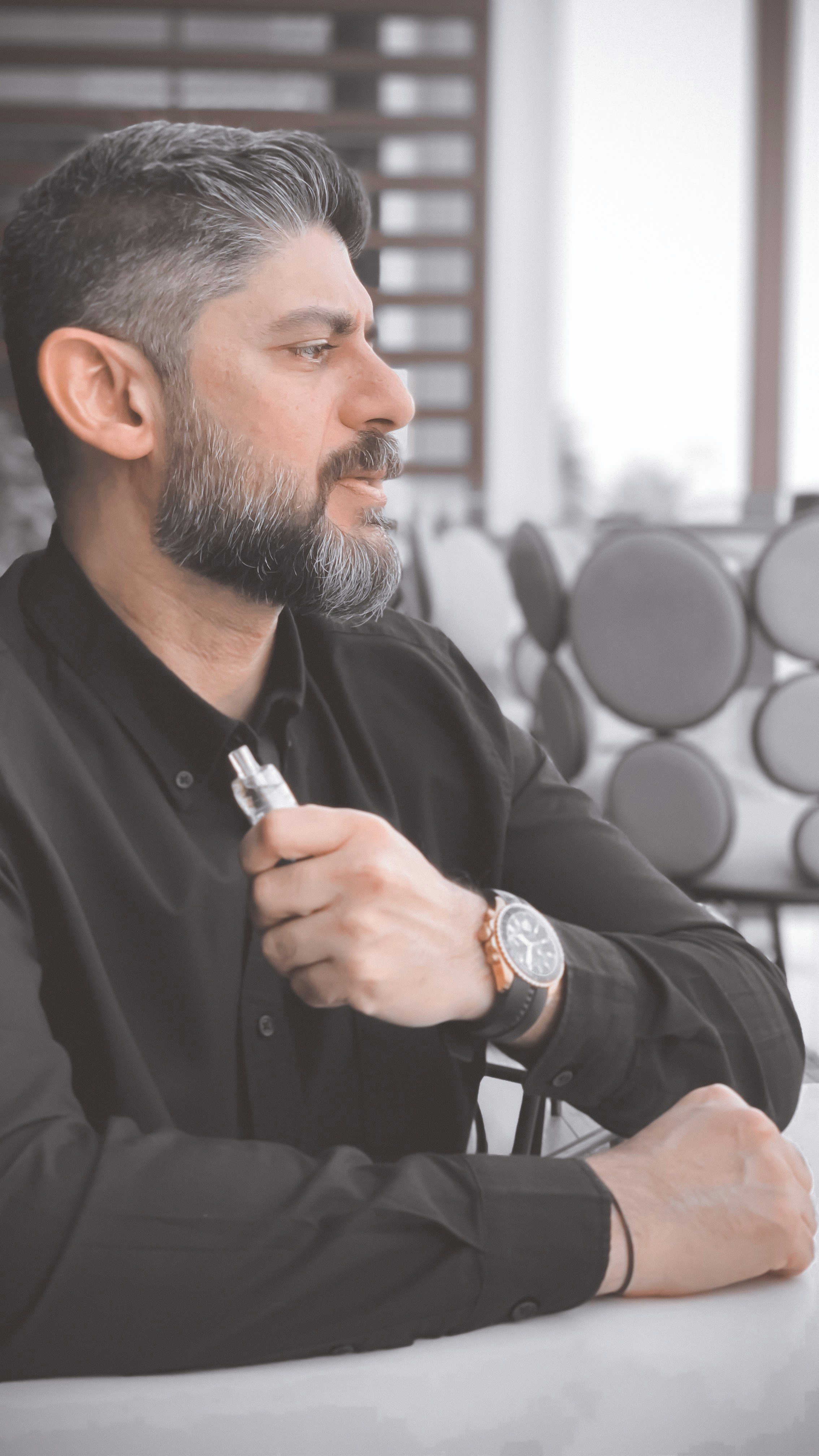 Man holding a vape device while sitting indoors in a modern setting.
