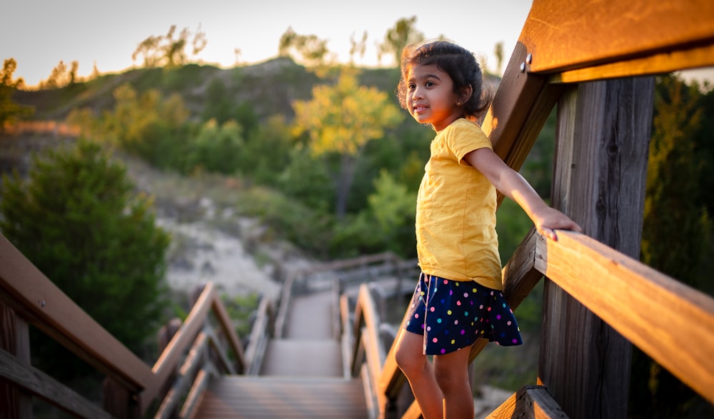 girl in yellow shirt and black and white skirt standing on brown wooden bridge during daytime