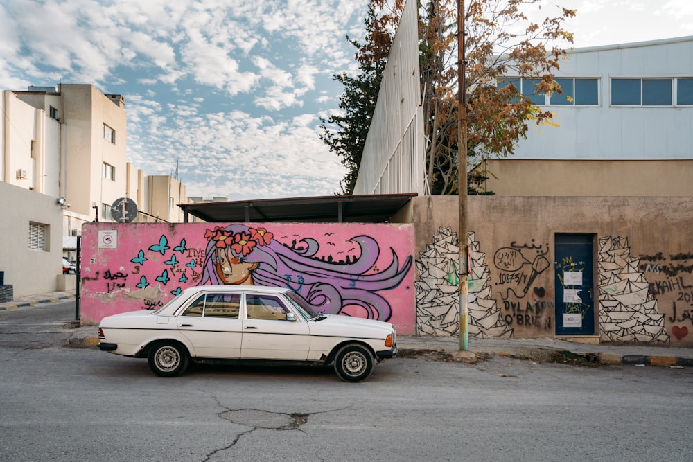 white sedan parked beside gray metal fence during daytime