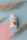 A white bottle with a red and orange label is positioned at the center. The label reads 'FENO GRAN PLUS' with additional text related to the product's natural ingredients. The bottle is surrounded by decorative dried grass stems, resting on a pastel blue background with a pink paper accent.