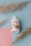 A white bottle with a red and orange label is positioned at the center. The label reads 'FENO GRAN PLUS' with additional text related to the product's natural ingredients. The bottle is surrounded by decorative dried grass stems, resting on a pastel blue background with a pink paper accent.