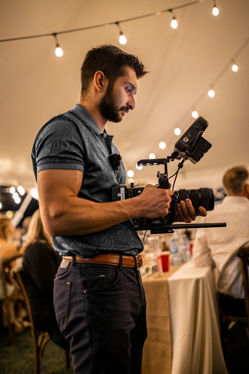 man in blue crew neck t-shirt and brown denim jeans holding black video camera