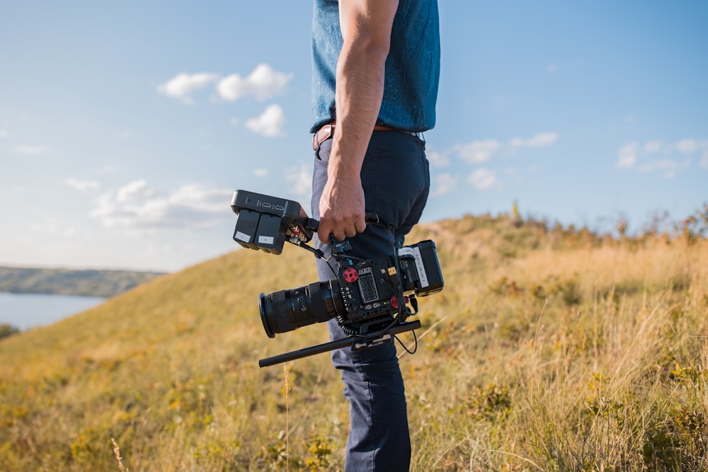 man in blue t-shirt and black pants holding black dslr camera