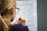 A person with long hair, wearing glasses, is focused on a worksheet with math problems related to measuring unknown perimeters. The individual is using a pencil to write or solve problems on the paper, which has various geometric shapes and equations printed on it.
