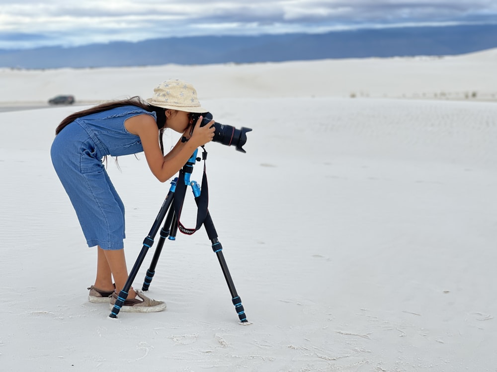 woman in blue t-shirt and white hat holding black dslr camera on white sand during