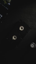 A vintage video cassette is placed on a dark surface, alongside part of a laptop keyboard in the top left corner and a watch in the bottom right. The lighting is dim and creates a moody atmosphere.