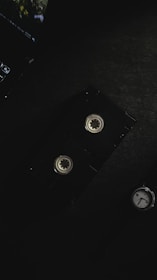 A vintage video cassette is placed on a dark surface, alongside part of a laptop keyboard in the top left corner and a watch in the bottom right. The lighting is dim and creates a moody atmosphere.