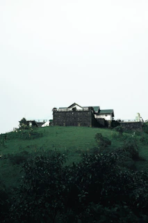 Sunlit exterior of a 3 BHK duplex villa surrounded by lush green hills under a clear blue sky.