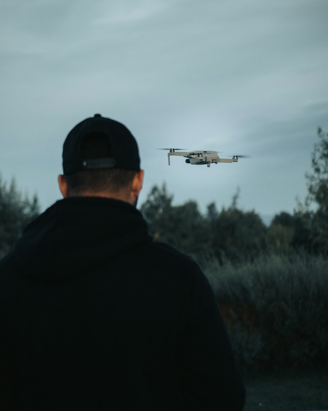man in black jacket and black cap looking at white drone