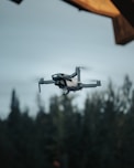 white drone flying over green trees during daytime