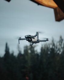 white drone flying over green trees during daytime