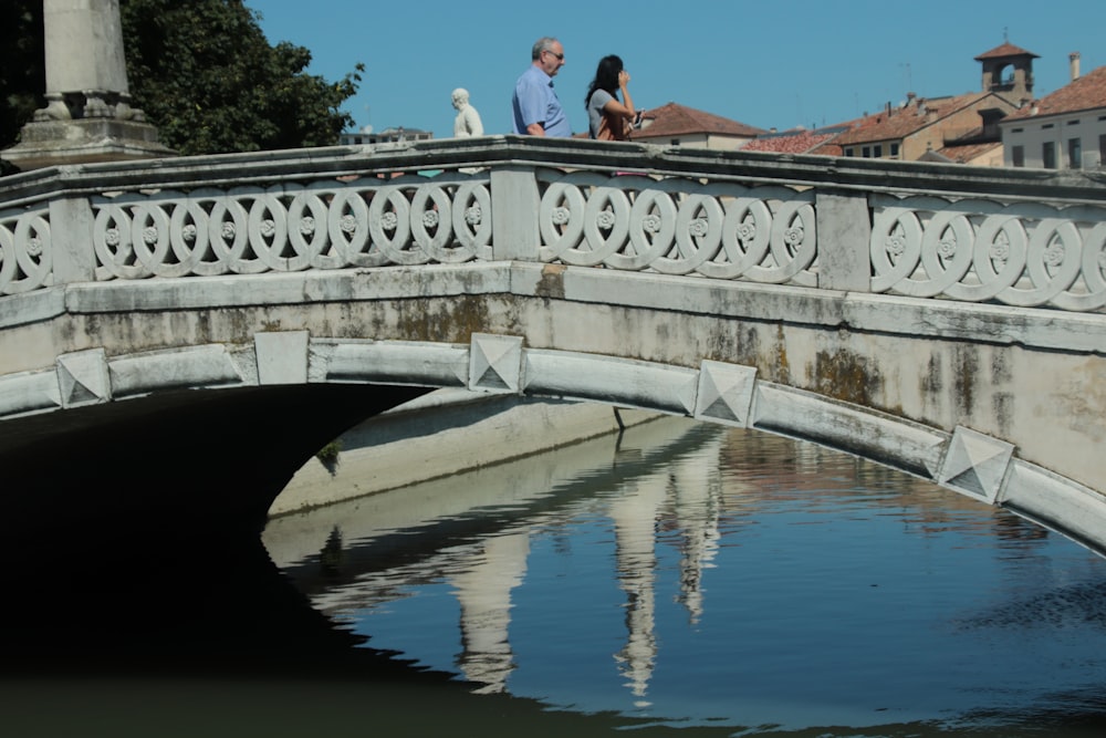 man and woman sitting on concrete bridge over river during daytime