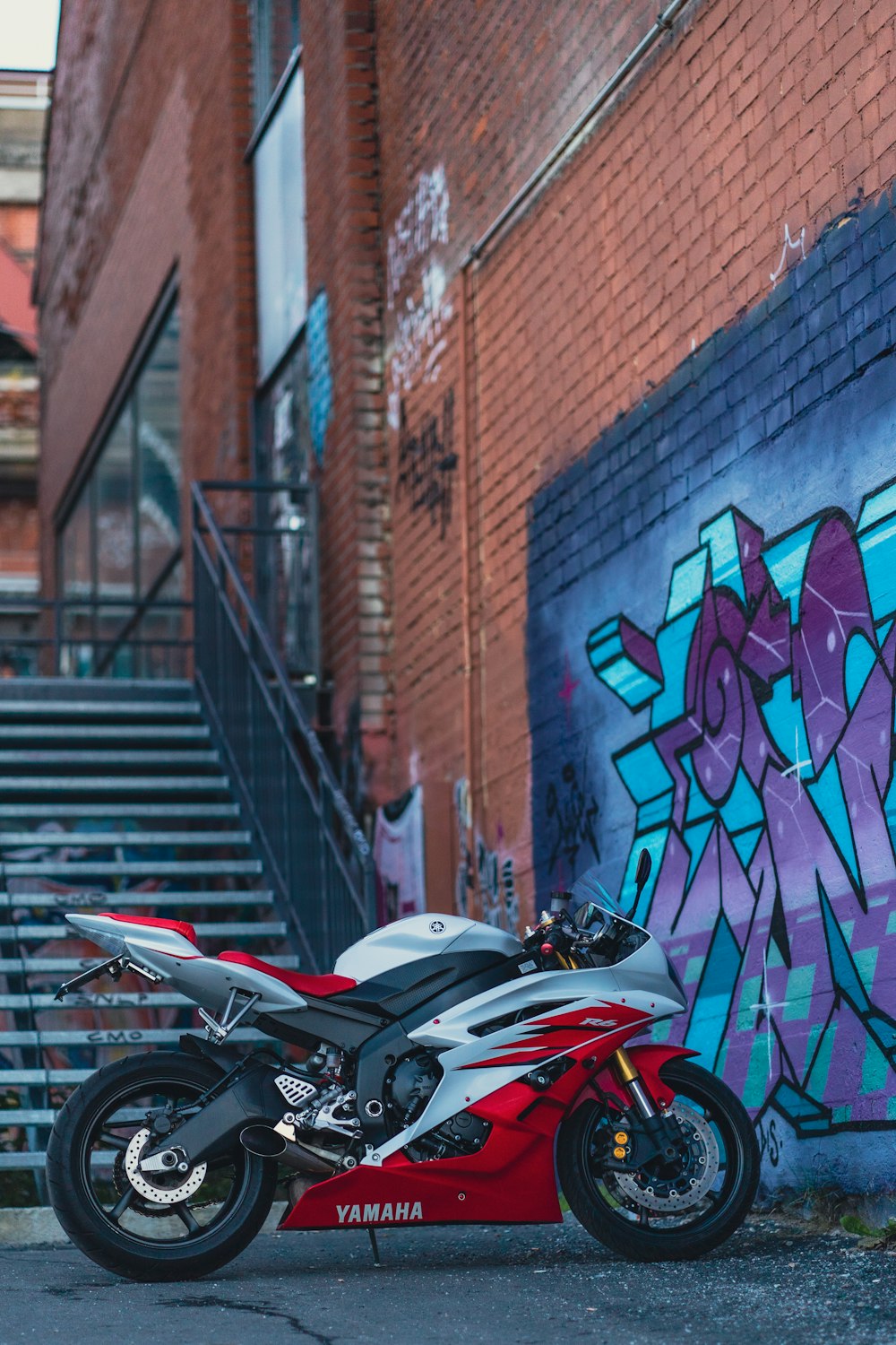 red and black sports bike parked beside brown brick wall
