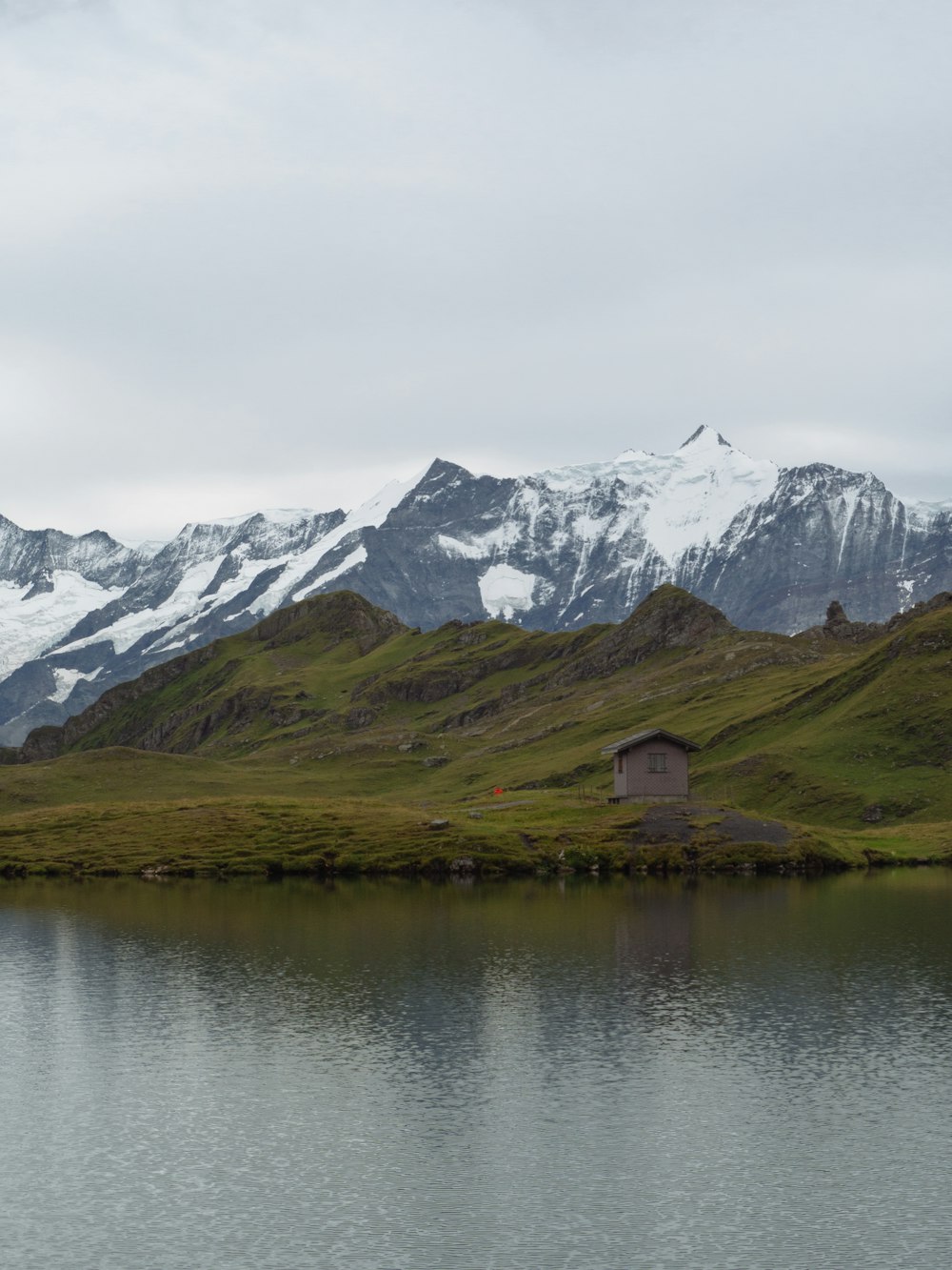 Maison en bois marron sur le lac près d’une montagne enneigée