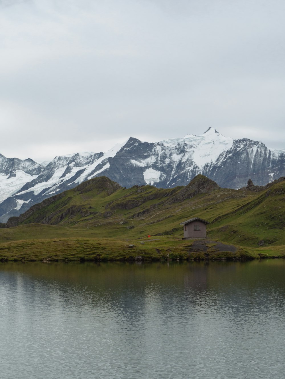 brown wooden house on lake near snow covered mountain