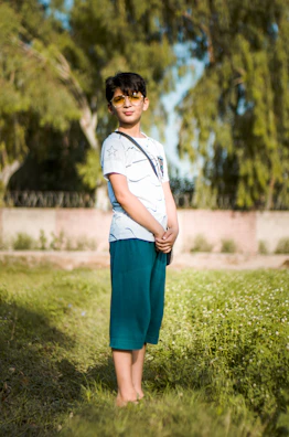 Boy wearing a crisp white shirt and lemon-toned shorts playing in a sunlit garden.