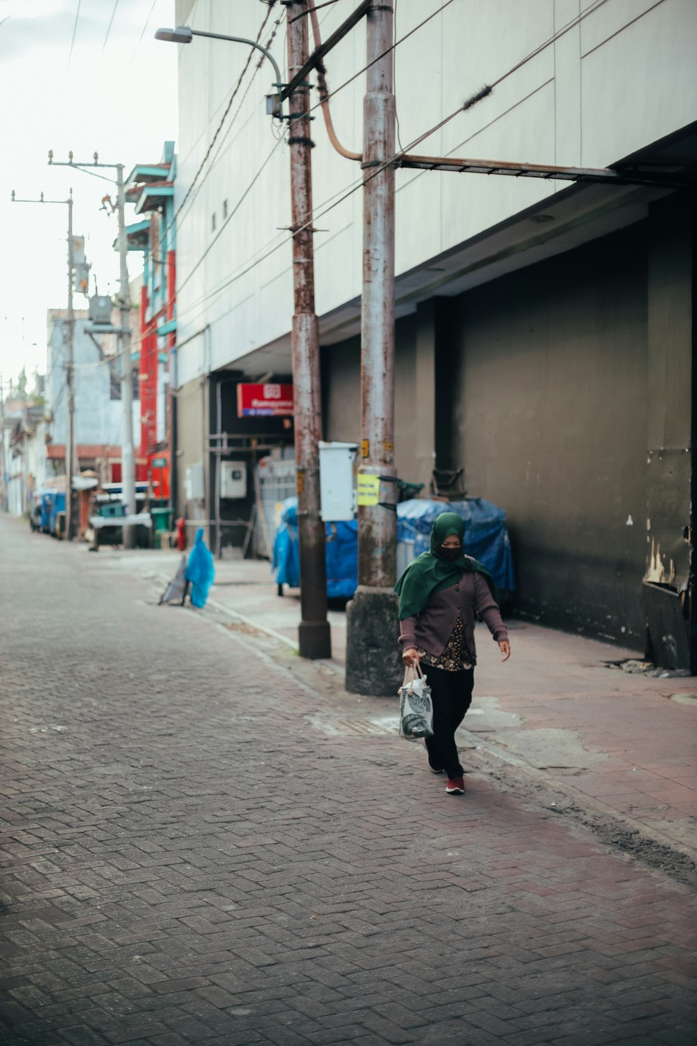 person in green jacket walking on sidewalk during daytime