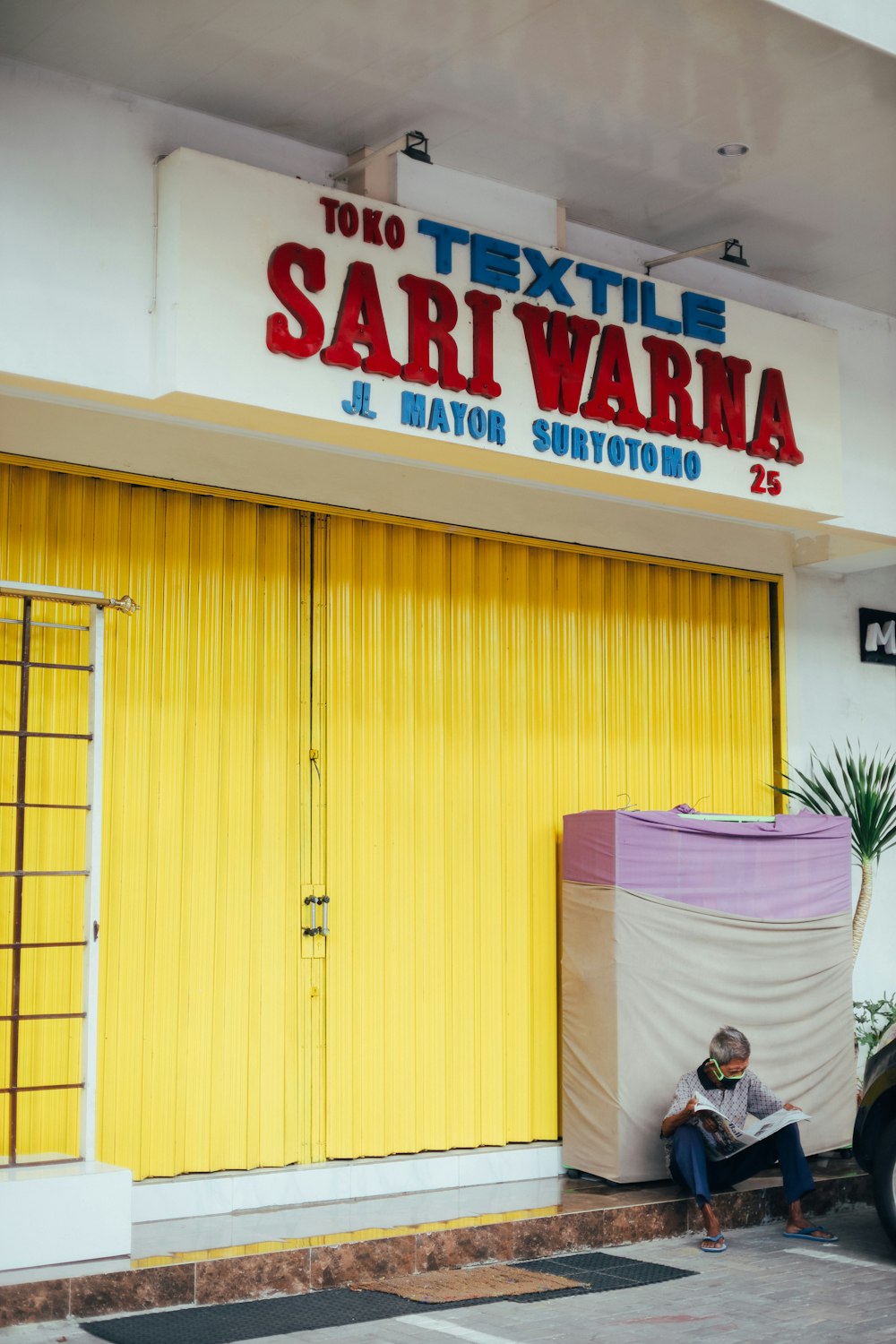 a man sitting outside of a store next to a yellow door