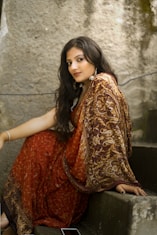 woman in red and gold sari dress sitting on gray concrete stairs