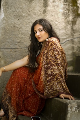 woman in red and gold sari dress sitting on gray concrete stairs