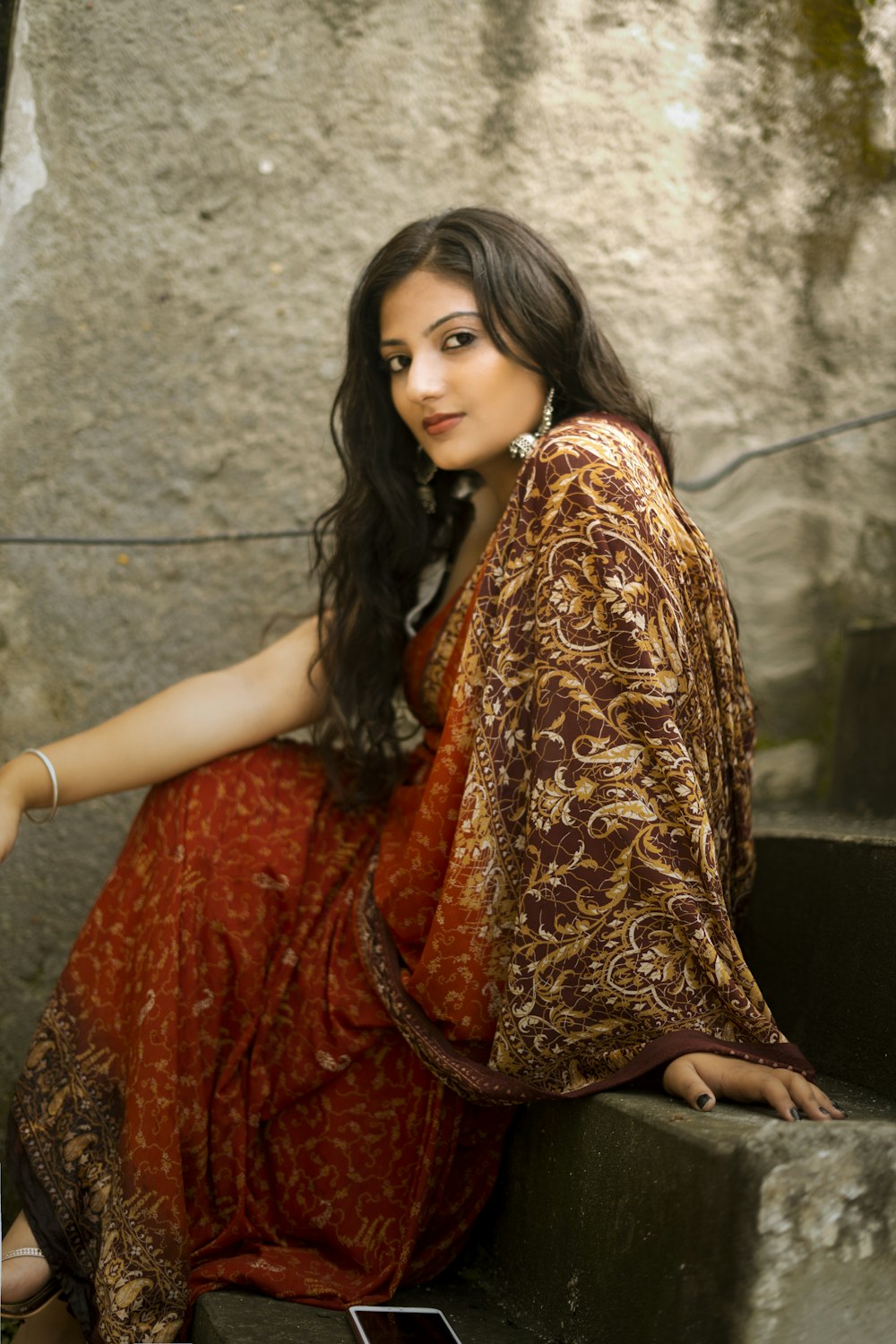 Donna in abito sari rosso e oro seduta su scale di cemento grigio