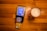 A payment terminal with a card inserted is placed on a wooden table next to a glass of beer on a colorful coaster. The terminal screen displays a payment request for 1.91 EUR.
