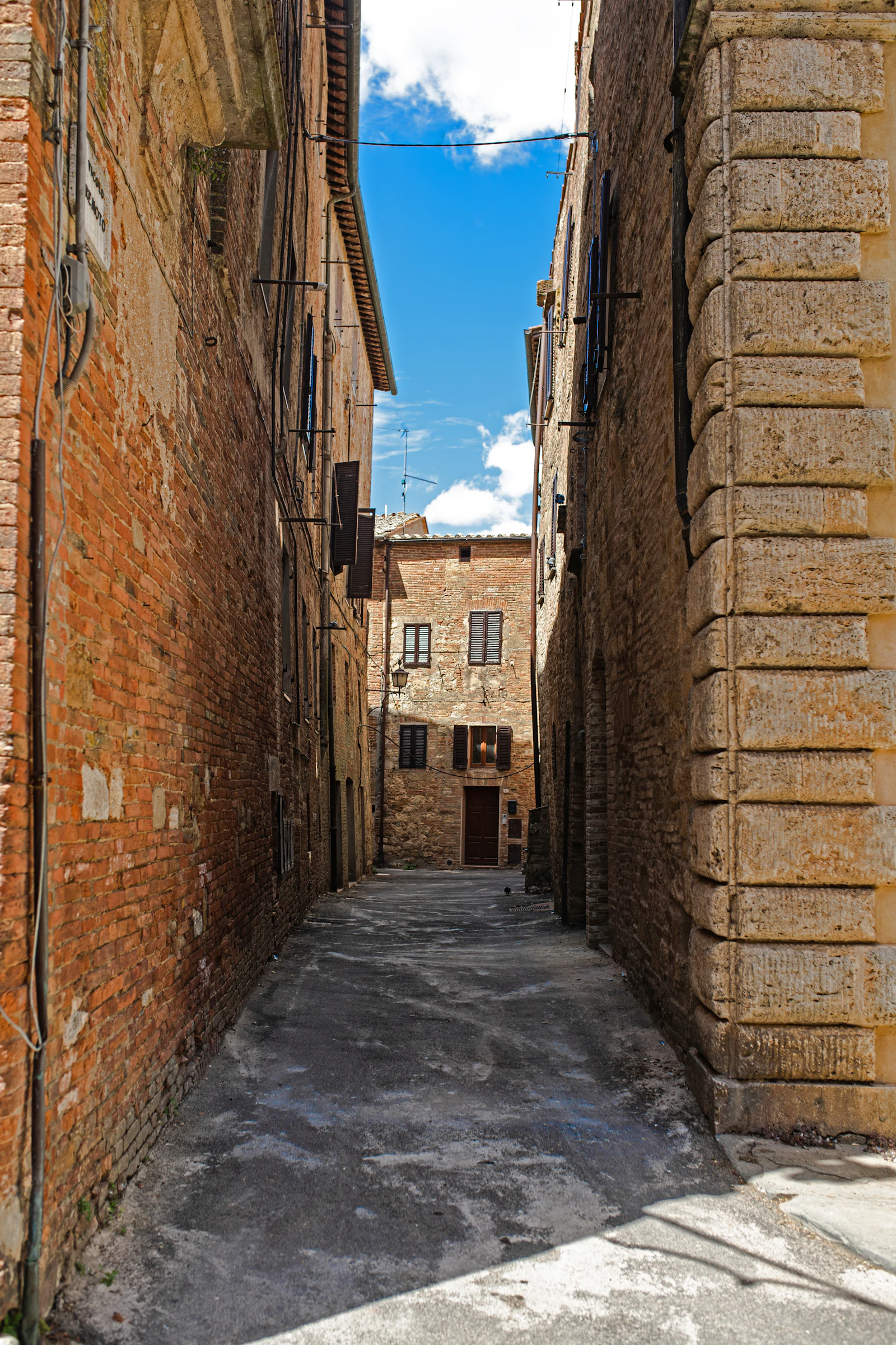 A narrow street climbs between stone buildings in Siena