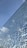 A cracked glass surface against a backdrop of a clear blue sky with a few clouds. The glass shows intricate patterns and reflections, giving an abstract aesthetic.