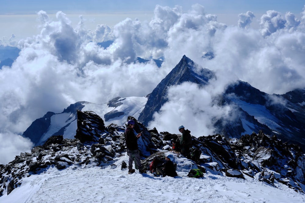 people sitting on snow covered ground near mountain under white clouds during daytime