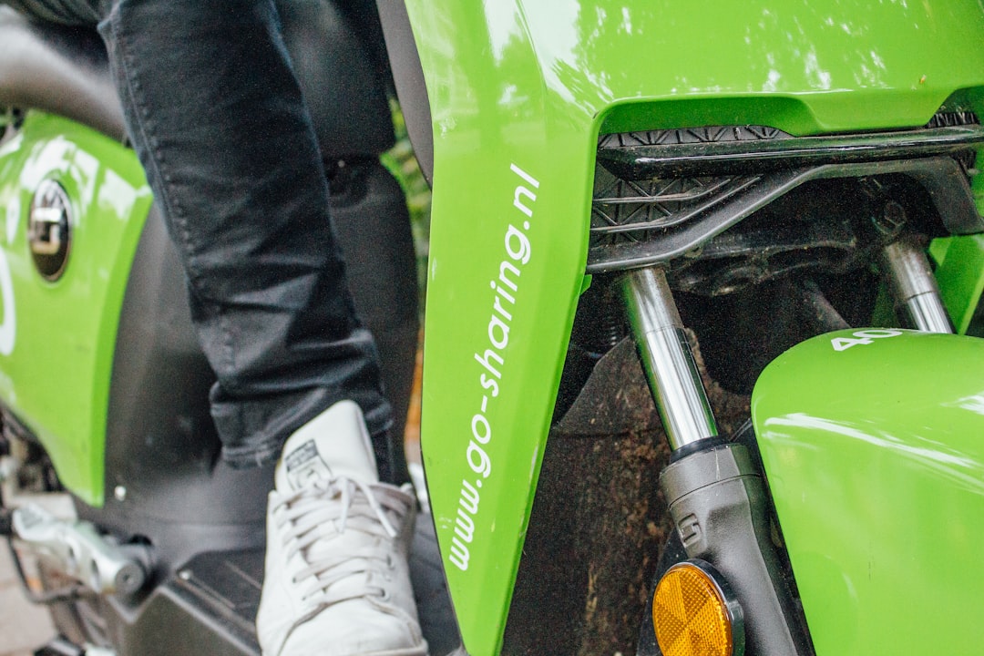 person in black jacket and white pants standing beside green motorcycle