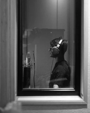 A monochrome shot of a person adjusting headphones in a minimalist recording studio.