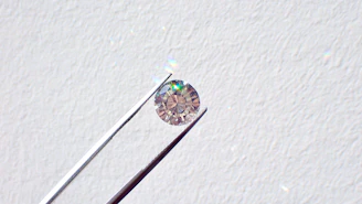 Close-up of a jeweler's hands inspecting a sparkling diamond with a magnifying loupe under bright light.