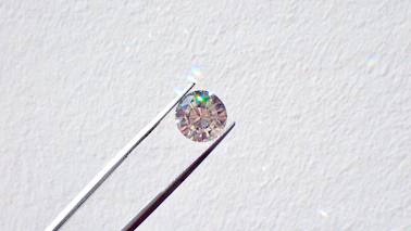 Close-up of a craftsman’s hands delicately examining a sparkling loose diamond under soft, warm light.