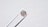 A single round diamond is delicately held by a pair of metal tweezers against a textured white background. The diamond sparkles with a spectrum of colors, highlighting its cut and clarity.