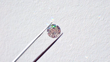 A close-up of a radiant fancy colored diamond sparkling under soft light on a light blue velvet background.