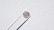 A single round diamond is delicately held by a pair of metal tweezers against a textured white background. The diamond sparkles with a spectrum of colors, highlighting its cut and clarity.