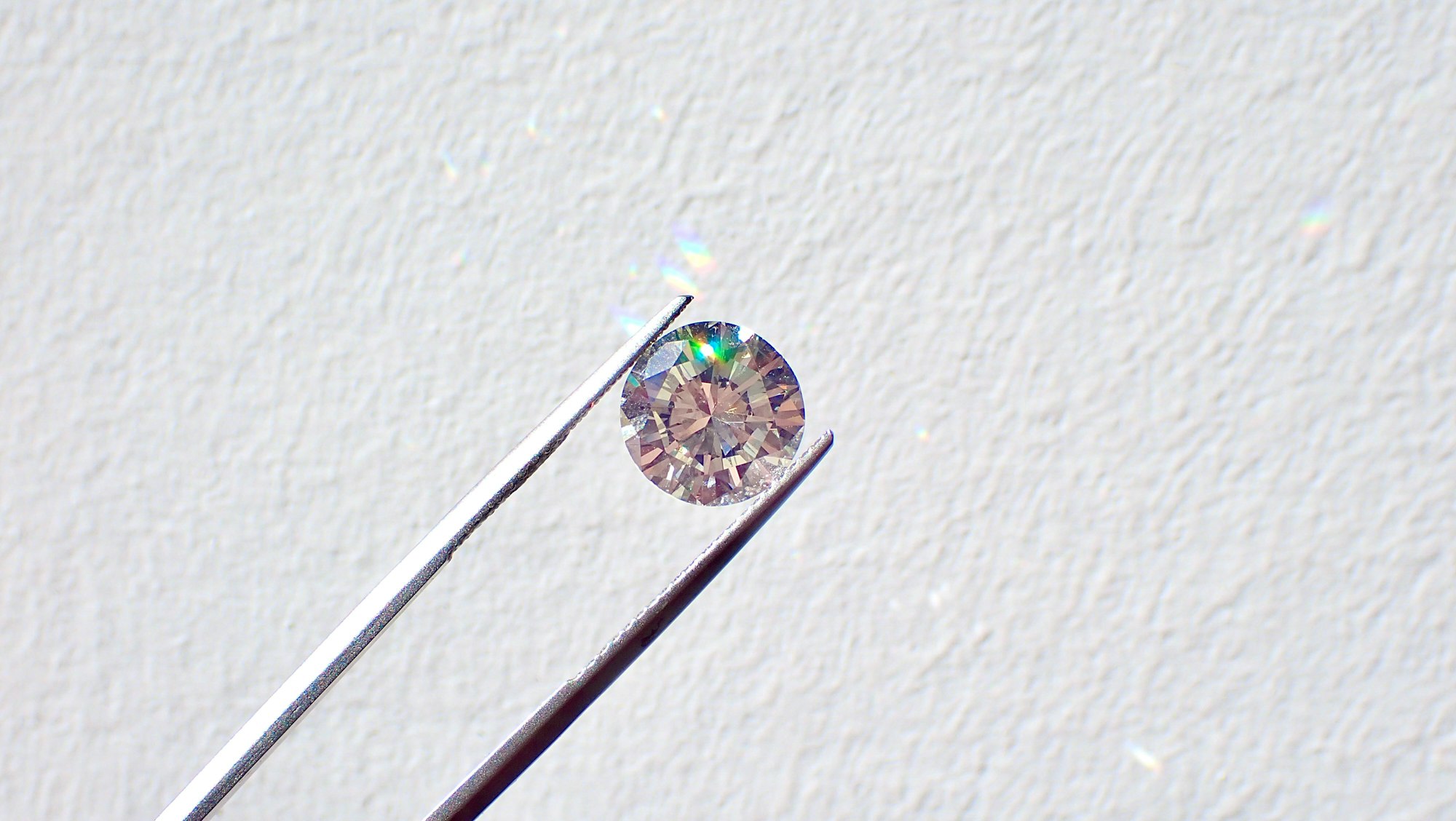 Diamond held between tweezers on a white wall