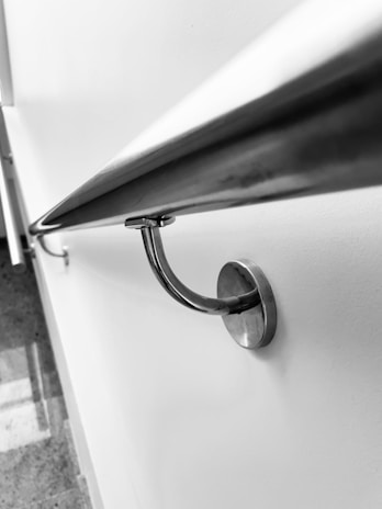 A sleek, metallic handrail is attached to a smooth white wall, with a reflective surface and curved design. The perspective is diagonal, creating a dynamic and modern feel.