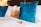 A neatly made bed with a set of blue velvet throw pillows and a small packaged brownie placed on the white bedspread. The background features a wooden headboard and soft, warm lighting, suggesting a cozy and inviting atmosphere.