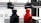 A 3D printer is in the process of printing two objects, one in black and one in red. The setup includes two extruder heads that are actively working on creating these cylindrical, industrial-like components. The printer is situated on a clean, white counter with visible branding and technical details in the background.
