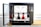 A modern 3D printer with an open door on the left, showcasing two spools of filament inside. The device is positioned on a wooden surface, with a black and metallic structure. The interior includes tubes and a printing head, with visible red and black filament on the printing platform.