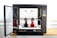 A modern 3D printer with an open door on the left, showcasing two spools of filament inside. The device is positioned on a wooden surface, with a black and metallic structure. The interior includes tubes and a printing head, with visible red and black filament on the printing platform.