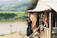 Smiling woman standing in front of a rustic rural house with greenery around.