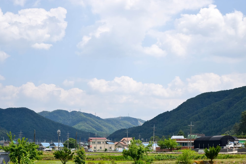 昼間、白い雲の下の緑の山の近くにある白と茶色のコンクリートの建物