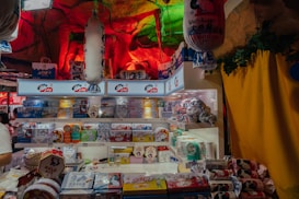 A store display featuring a variety of White Rabbit branded products. The shelves are filled with colorful packaging displaying images of rabbits and logos. The background has a cave-like appearance with red and green lighting, giving an atmospheric feel. Decorative elements like hanging lanterns and leafy accents add to the visual interest.