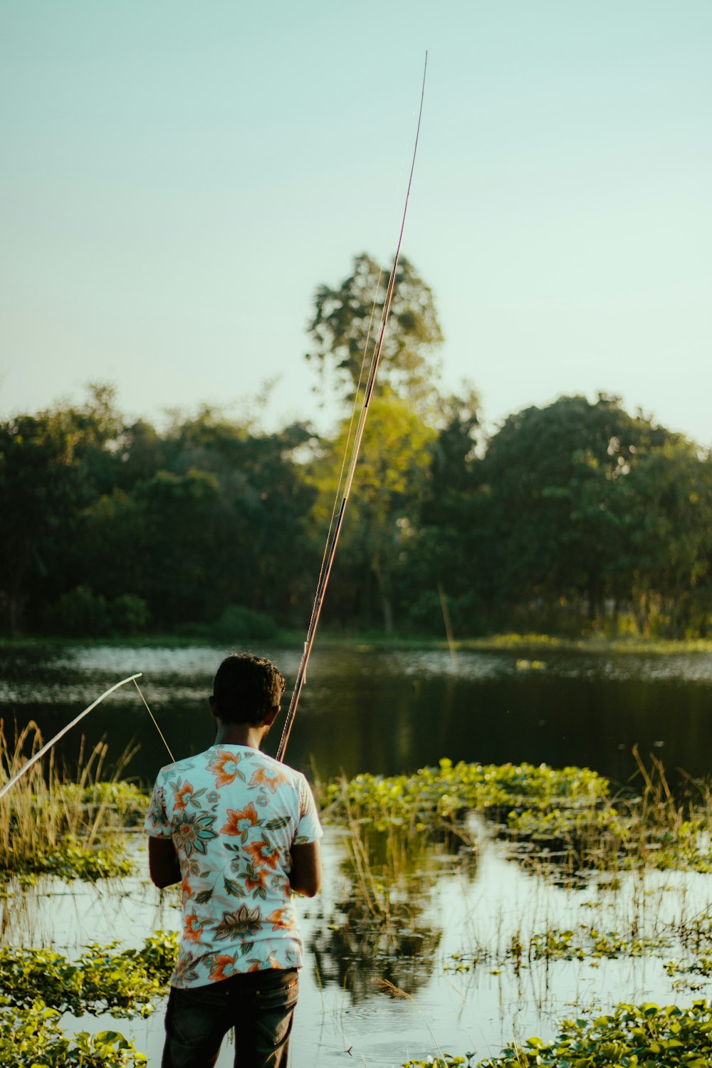 man in white shirt fishing on lake during daytime