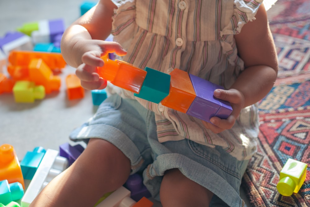 파란색과 주황색 플라스틱 장난감을 들고 있는 갈색 버튼 업 셔츠를 입은 소녀