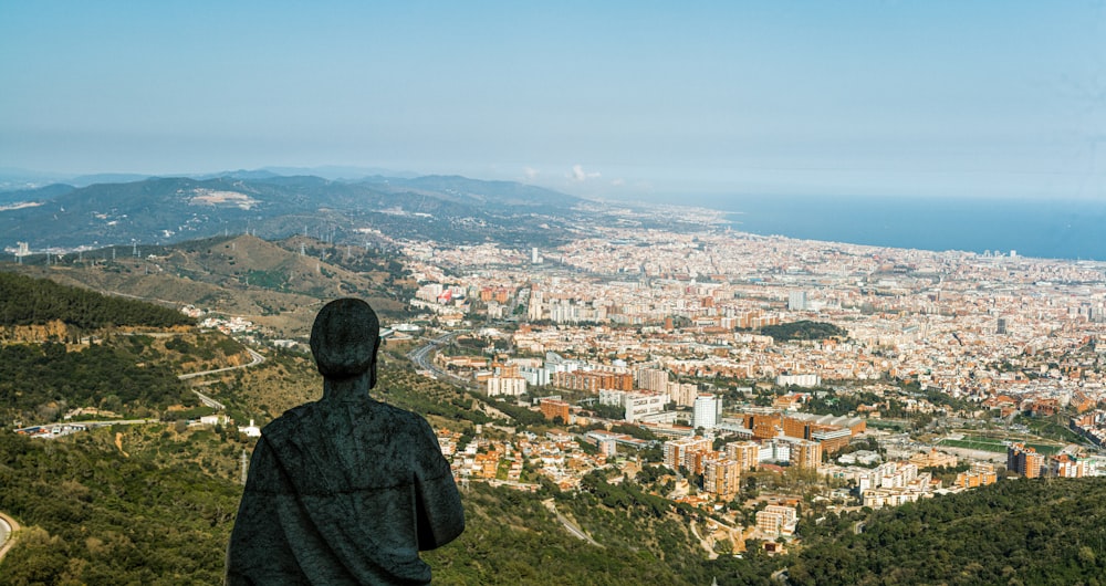 hombre con sudadera con capucha negra de pie en la cima de la montaña mirando la ciudad durante el día