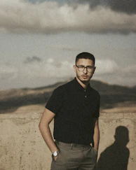 a man with glasses standing in front of a wall